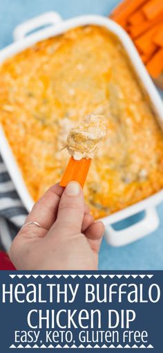 a person holding up a piece of chicken dip in front of a casserole dish