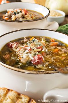 two white bowls filled with soup on top of a table next to bread and vegetables