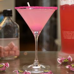 a pink drink in a martini glass with candy candies around the rim and bottles behind it