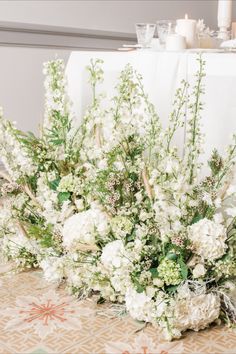 white flowers and greenery are arranged on a table cloth at a wedding reception with candles in the background