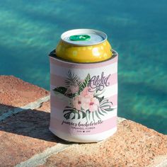 a can of beer sitting on top of a rock near the water