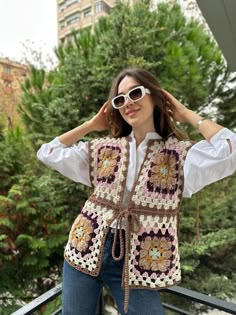 a woman wearing sunglasses and a crocheted vest is posing for the camera with her hands on her head