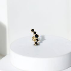 a gold ring with black stones sits on top of a white pedestal in front of a white wall