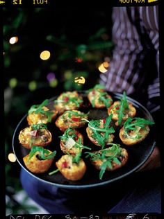 a person holding a plate full of small appetizers in front of a christmas tree