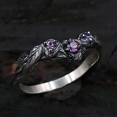 a silver ring with two purple stones in it on top of a stone slabd surface