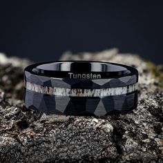 a black and white ring with the word tunsten on it sitting on top of some rocks