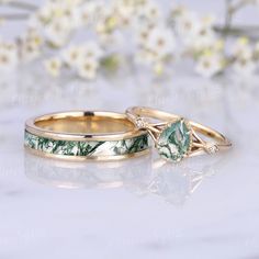 two gold wedding rings with green and white marble inlays sitting on top of each other