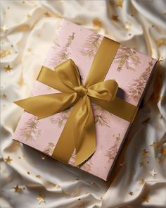 a pink and gold wrapped gift box with a bow on it's side sitting on a bed