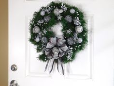 a christmas wreath hanging on the front door with silver and white ornaments around it,