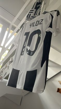 a soccer jersey hanging from the ceiling in front of a window with white and black stripes