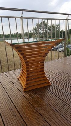 a wooden table sitting on top of a wooden deck next to a metal railing with cars parked in the background