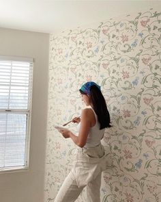 a woman standing in front of a wallpapered wall using a paint roller to paint the walls