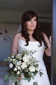 a woman in a white dress holding a bouquet and looking at the camera while standing next to an open door