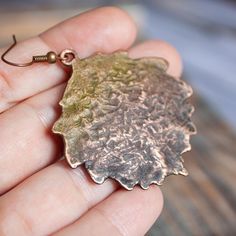 a hand holding a bronze leaf shaped pendant