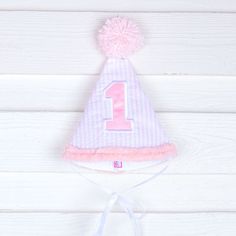 Happy 1st birthday to your little one! This cone hat with a pom pom on top is perfect for cake smashing pictures and first birthday celebrations. Your little one will look so adorable in this darling hat styled to match their big day! Cute Adjustable Hat For First Birthday, Cute White Hat For First Birthday, Playful Mini Hats For Birthday, Playful Adjustable Mini Hats For Birthday, Fun Birthday Party Hat Supplies, Playful Adjustable Hats For Birthday, Fun Pink Birthday Hat, Cute Pink First Birthday Party Supplies, Playful Pink Mini Hats For Birthdays