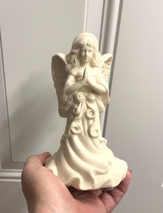 a hand holding a small white angel statue