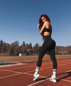 a woman with red hair wearing black sports bra and leggings standing on a tennis court