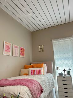 a bedroom with a bed, dresser and two pictures hanging on the wall above it