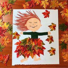 a child's drawing of a girl surrounded by autumn leaves on a wooden table