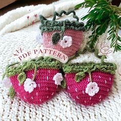 two crocheted strawberries sitting on top of a blanket next to a plant