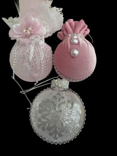 three pink and white christmas ornaments on a black background, one with a flower in the center