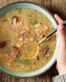 a bowl of bean and ham hock stew on a wooden table with a spoon in it