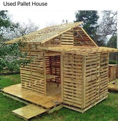 a small wooden house made out of wood pallets on the grass with trees in the background