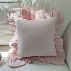 a white pillow with pink ruffles on it sitting on top of a couch