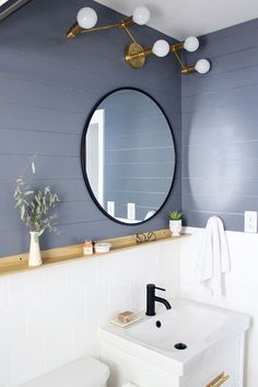 a white toilet sitting next to a bathroom sink under a round mirror on the wall