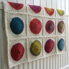 a crocheted wall hanging on the side of a white wall with multicolored balls