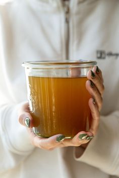 a woman holding a cup of tea in her hands with green nail polish on it