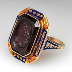 This unique and special circa 1900 Victorian intaglio ring features engraved details along the top and side faces with blue and orange enamel. The ring is accented with one (1) bezel set cut-cornered rectangular shaped intaglio cut garnet. The ring measures 20.7mm at the top, rises 6.5mm above the finger, tapering to 1.6mm wide and 1.0mm thick at the base of the shank. It is a size 4.75 and we are not offering resizing due to the enamel on the ring. It shows average wear for its age. Antique Yellow Gold Enamel Ring, Antique Enamel Rings For Formal Occasions, Vintage Enamel Cabochon Rings, Antique Oval Enamel Ring Collectible, Victorian Oval Enamel Rings, Art Deco Yellow Gold Enamel Ring For Formal Occasions, Antique Engraved Enamel Ring For Formal Occasions, Art Deco Formal Yellow Gold Enamel Ring, Formal Yellow Gold Art Deco Enamel Ring