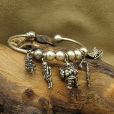 This vintage charm bracelet is a beautiful addition to any Christmas jewelry collection. The bracelet is made from sterling silver and features a classic charm style. The cuff has an inside measurement of 6" with an additional 9/16" gap. The charms include a Christmas tree (20mm x 9.5mm), nutcracker (23.5mm x 8mm), Santa Clause ( 24mm x 12mm), candy cane (25mm x 8mm), and a sleigh (15mm x 14mm). There is no artist's hallmark or stamp on the piece. There is also the ability to add on more charms Collectible Silver Christmas Jewelry, Silver Hallmark Jewelry For Christmas, Christmas Silver Hallmark Jewelry, Silver Charm Bracelet For Christmas, Vintage Silver Bangle Charm Bracelet, Classic Charm Bracelet With Vintage Charm As Gift, Silver Charm Bracelets For Christmas, Vintage Charm Bracelet, Santa Clause