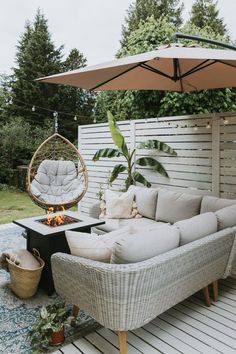 a couch and chair on a deck with an umbrella over the fire pit in the back yard