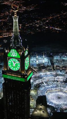 a large clock tower in the middle of a city at night with lights all around it