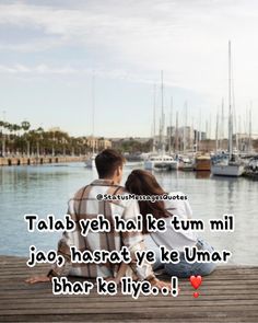 two people sitting on a dock with boats in the background