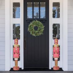 two nutcrackers standing in front of a black door with a wreath on it