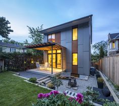 a modern house is lit up at night in the back yard with flowers and trees