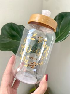 a hand holding a clear and yellow water bottle next to a green leafy plant