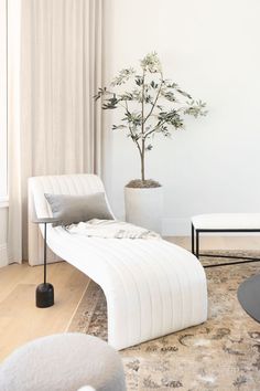 a white chaise lounge chair sitting next to a potted tree in a living room