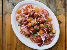 a white plate topped with lots of tomatoes and onions on top of a wooden table