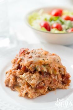 a white plate topped with lasagna next to a bowl of salad