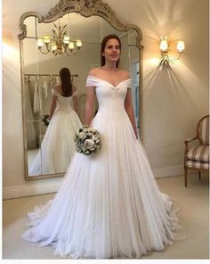 a woman standing in front of a mirror wearing a wedding dress with off the shoulder sleeves