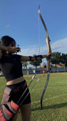 a woman in black shirt and shorts holding up a bow with two arrows on it