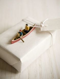 two people in a small boat on a white cloth covered gift box with twine