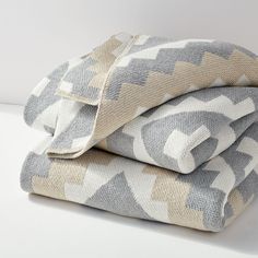 two blankets folded on top of each other in grey and white colors with geometric designs