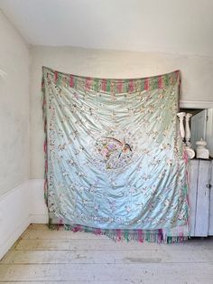 an old curtain is hanging in the corner of a room with white walls and flooring