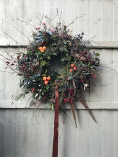 a wreath hanging on the side of a building with berries, leaves and other foliage