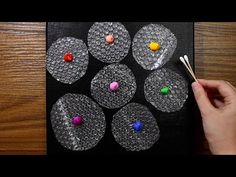 a person is holding a paintbrush and painting circles on a piece of black paper