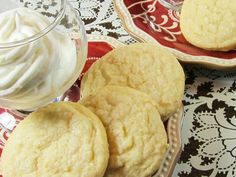 three cookies and whipped cream on a red plate next to a glass bowl with white frosting